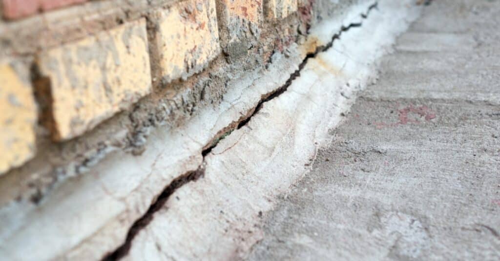 Close-up of a yellow brick wall and a concrete surface. A long crack runs along the base where the two meet.