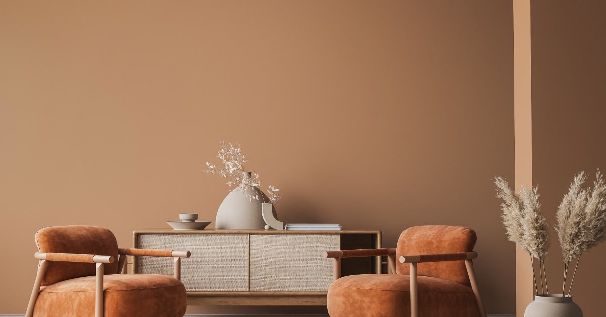 Two orange-brown armchairs sit in front of a low cabinet against a warm brown wall. A circular rug is between them.