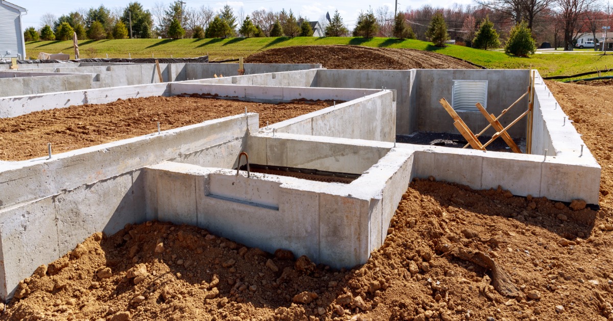 New concrete foundation walls sit within an excavated residential lot. Exposed soil surrounds the foundation.